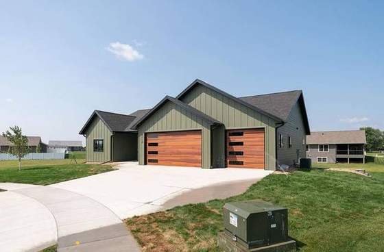 Green board-and-batten ranch with cedar-tone garage doors